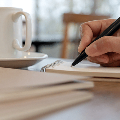 A hand writing in a notebook with a pen