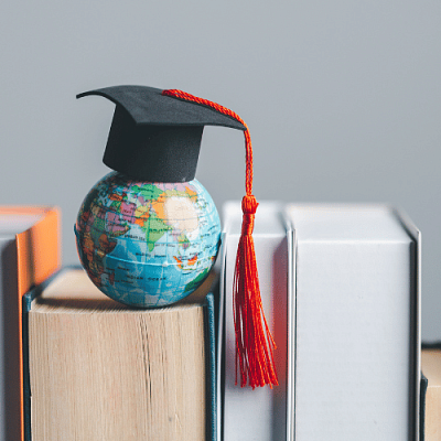 A mini globe wearing a graduation cap on top of a stack of books
