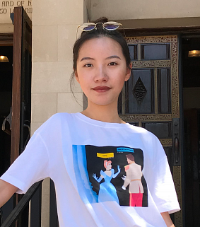 Asian woman with glasses on her head and a colorful T-shirt looks at the camera; wooden doors visible behind her.