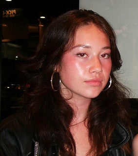 Young white woman with long brown hair, large hoop earrings and a black top