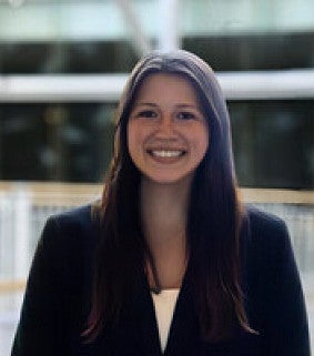 Young woman with long brown hair wearing a blazer and smiling at the camera