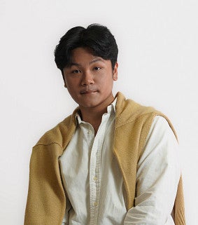 Young Thai man with dark hair wearing a white shirt and cream pullover draped over his shoulders