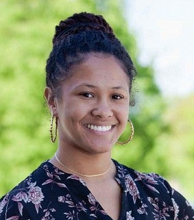 African American woman with her hair up, gold hoop earrings, and a black-and-purple top smiles at the camera