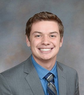 Man with short brown hair, blue shirt and tie, and grey suit