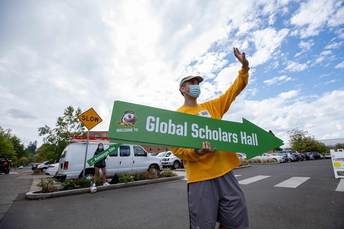 Student Volunteer waves and holds a sign that points towards Global Scholars Hall