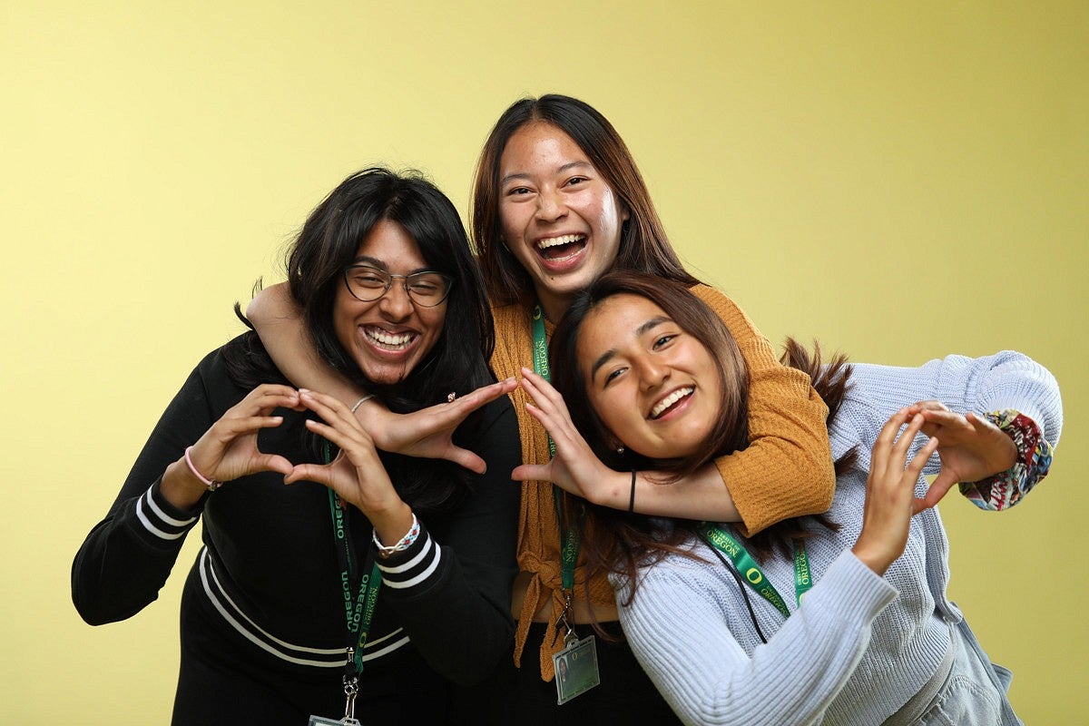 three students hugging and making the University of Oregon O hand gesture