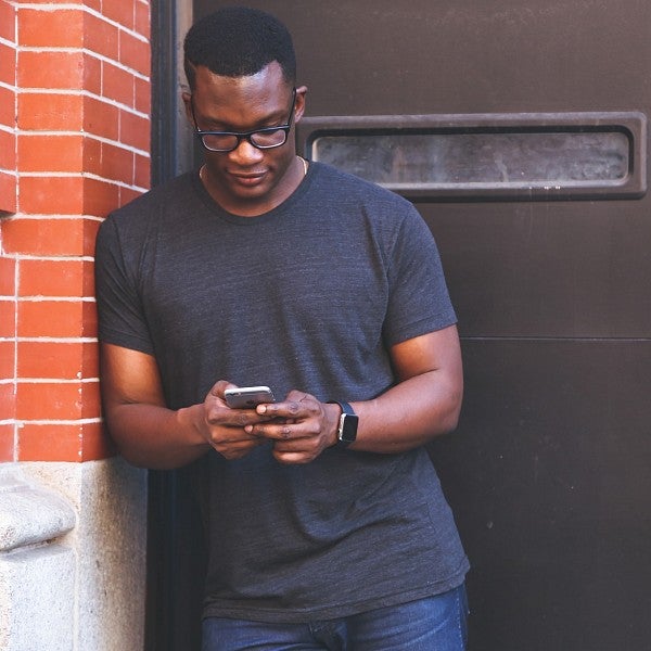 Student leans on building while using smartphone
