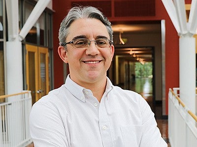 Joshua Skov headshot. Joshua is smiling, has grey hair and glasses, and is wearing a white collared shirt.