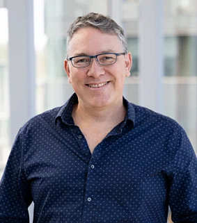 Paul Dalton smiling with short gray hair and glasses, wearing a navy, collared shirt.