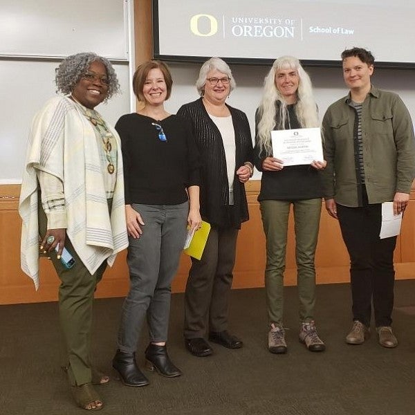 Megan Austin smiling and holding certificate, standing onstage with smiling AEC and School of Law staff.