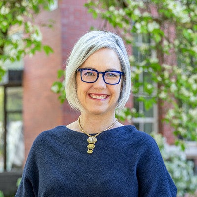Kate Mondloch headshot. Kate is smiling, has short grey hair and purple glasses, and is wearing a blue sweater.