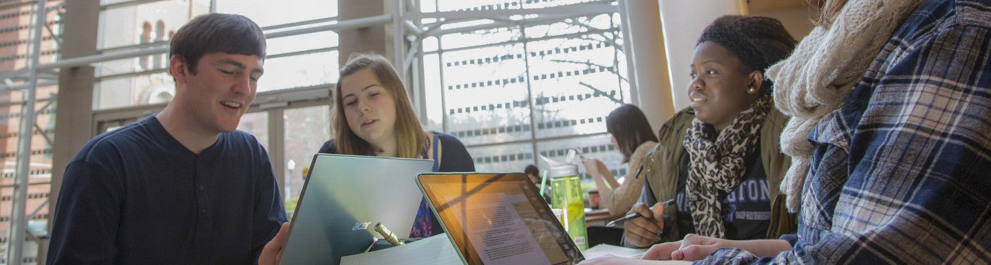Four students sitting at a table with laptops working on a project