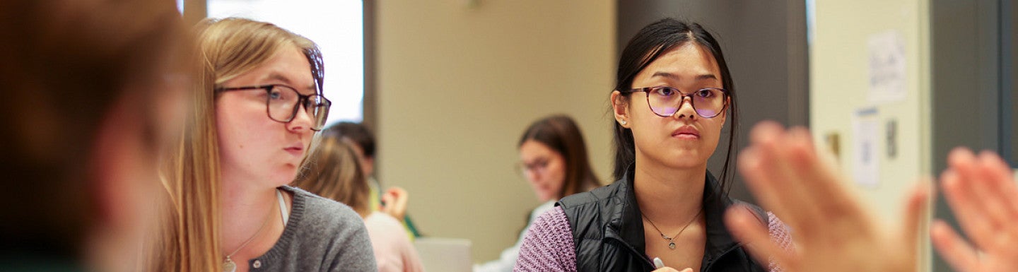 Two students sitting at a table looking at someone across from them.