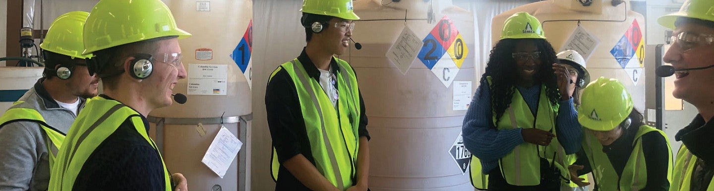 Members of the Net Impact group laugh together while wearing reflective vests and hard hats during a site visit