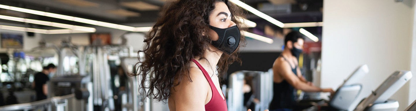 A person exercises on a gym treadmill while wearing a mask