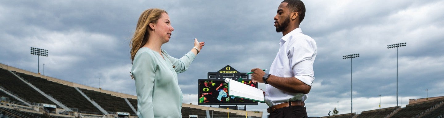 Two students talk on the field of a sports arena