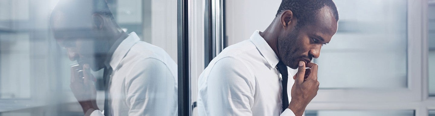 A man sits against a glass wall in thought