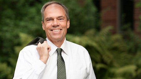 Headshot photo of Bruce Blonigen smiling at the camera wearing a white shirt with a brown tie with his suit jacket thrown over his right shoulder