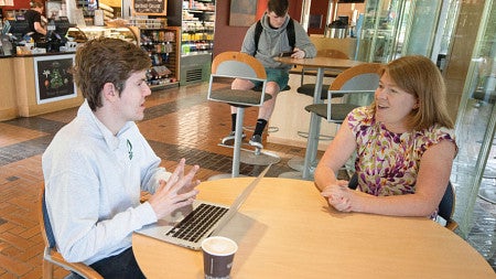 Photo of professor Lanahan meeting with a student while sitting at a round table in the cafe inside the Lillis Business Complex