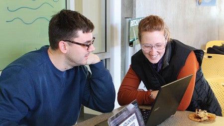 Three students sitting together at a table compare notes on their laptops.