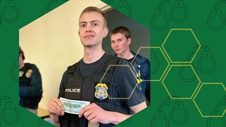 A student wearing a police vest participates in a mock fraud investigation during a simulated exercise.