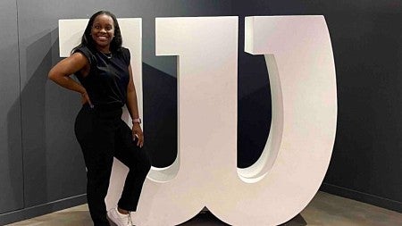 Mufaro Hungwe stands in front of a 3D "W" from the Wilson company's logo. On the wall behind her is the quote "Nobody who ever gave their best regretted it. George Halas"
