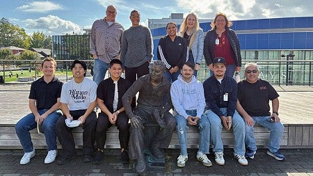 SPM students and faculty pose for a group photo around a statue