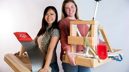 Morgan Nguyen (left) and Kailey Chaffee (right) stand back-to-back while holding up their new launching devices to help Special Olympians compete in cornhole events