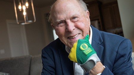 Alan Eliason braces his chin with his fist while wearing a UO College of Education glove