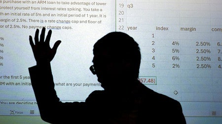 Calvin Zhang is shown backlit in front of a projection screen as he teaches a real estate finance class