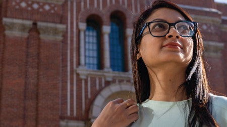 Iffat Rabbani looks up at blue sky above her. A brick building on UO campus is behind her.
