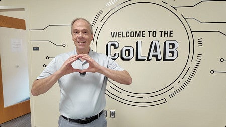 Dean Bruce Blonigen stands in front of a wall mural with the text -Welcome to the CoLAB-
