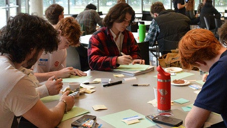 Students participating in the Oregon Innovation Challenge write on post-it notes during an activity
