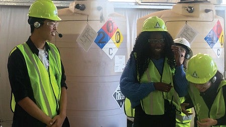 Members of the Net Impact group laugh together while wearing reflective vests and hard hats during a site visit