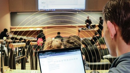 A student takes notes on his laptop during class in a large auditorium