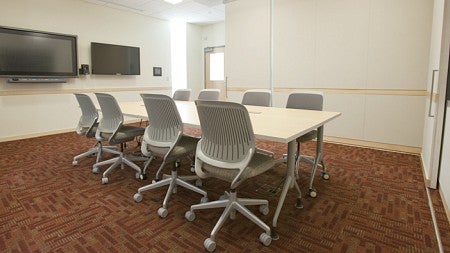 The inside of the ESI lab showing a conference table with eight chairs and two large tv screens on the wall