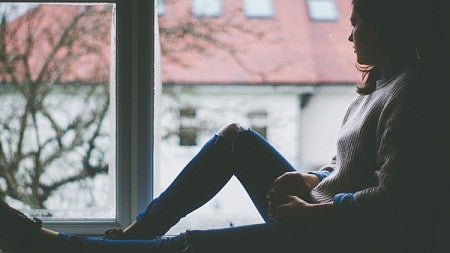 A woman sits on a window sill on a rainy day and looks outside