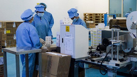 Workers in scrubs work on a factory floor