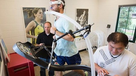Man runs on treadmill while two others take notes.