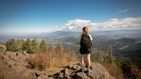Student stands on rock overlooking Eugene from the top of a hike