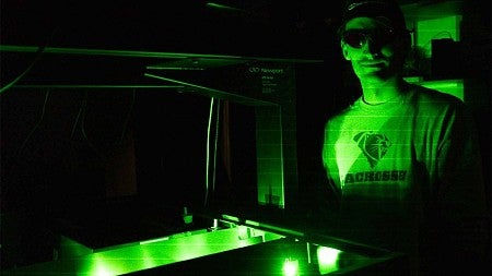 A student in  lab wearing goggles illuminated by green laser