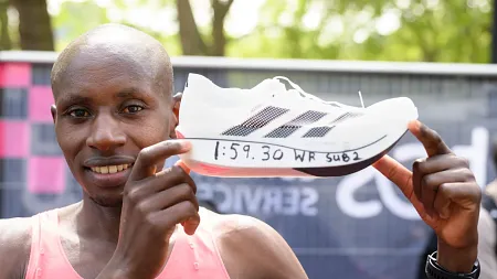 a man holds up a shoe with 1:59:30 written on it 