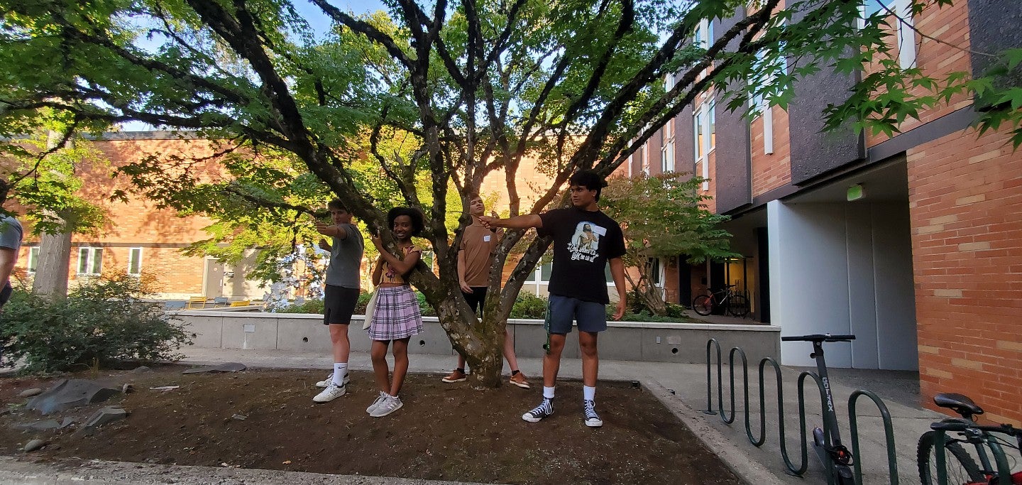 Four students pose in front of a tree in the Justice Bean Hall courtyard