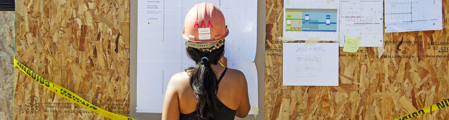 BDI photo of a student in front of a building diagram on a construction site. 