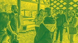 Photograph of students eating pizza outside with the College of Design Dean, Adrian Parr. Photo is done in a duotone style with green shadows and yellow highlights.