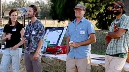 four people standing in front of a table outside in the grass