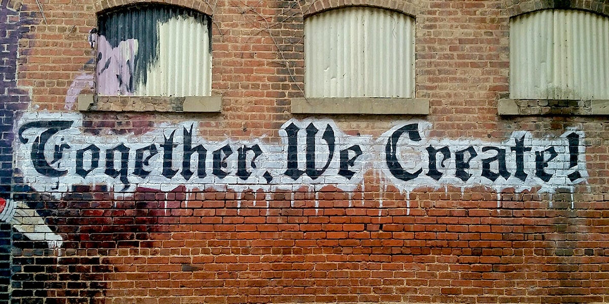 Graffiti that says Together We Create on brick wall