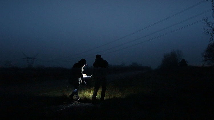 click to enlarge two people in the dark with flashlight in field under power lines