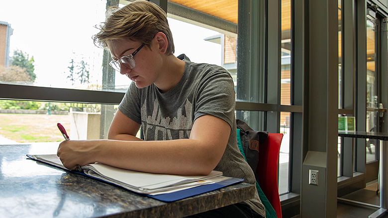 image of student with an open book sitting at a table and writing