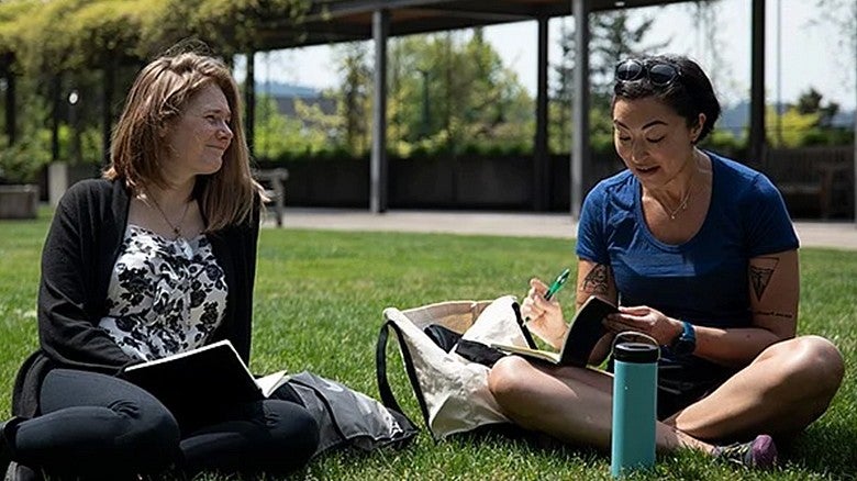 two students sitting in the grass outdoors in HEDCO